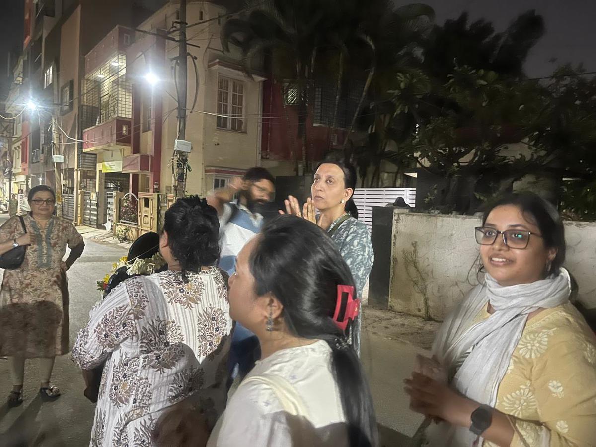 Walkers gathered on a quiet residential lane at night, listening before the kirtan begins